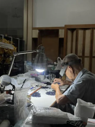 A cutter at his bench under a single lamp sorting small blue sapphires