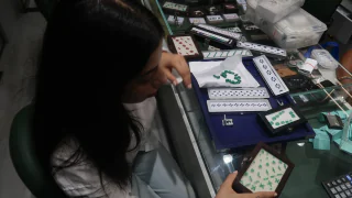 Seen from above, a buyer at a glass counter with trays of emeralds open in front of her