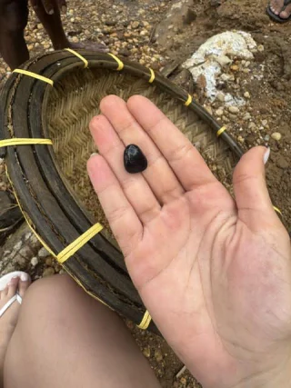 A rough dark stone resting in an open palm beside a woven sieve