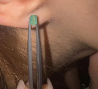 An emerald held in tweezers against the ear