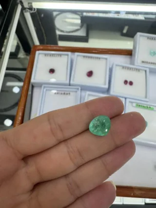 An emerald held in the hand beside labelled stone boxes